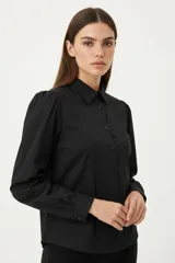 Camisa negra de poliéster con cuello clásico, cierre frontal de botones y mangas largas con sutiles frunces en los hombros.