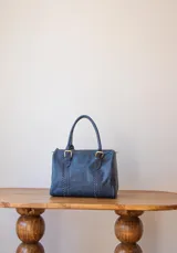 Bolso de mano azul con detalles de costuras verticales y herrajes dorados.