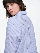 Camisa de dormir de popelina de algodón, con estampado de rayas verticales y pequeños motivos geométricos. Presenta cuello camisero, mangas largas y cierre frontal mediante lazos ajustables.