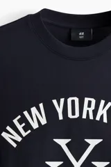 Remera de algodón color negro con cuello redondo acanalado, mangas cortas y hombros caídos. Presenta un estampado frontal en color blanco con la inscripción New York City y un monograma central.