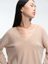 Sweater de punto gris con escote en V profundo, hombros caídos y mangas largas. Presenta un diseño de calce relajado con sutiles micro lentejuelas integradas en el tejido.