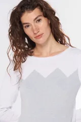 Buzo de tejido de punto con diseño bicolor, combinando blanco en la parte superior y mangas con un tono celeste grisáceo en el cuerpo, presentando un patrón geométrico en la unión de los colores. Posee cuello redondo y mangas largas.