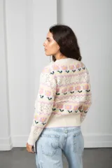 Cárdigan de punto color crema con diseño de flores en tonos rosados y verdes, guardas caladas, escote en V, cierre frontal con botones y terminaciones acanaladas.