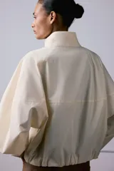 Camisa de cuello subido y manga larga con puños elásticos. Diseño holgado con cierre frontal de botones ocultos por solapa.
