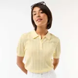 Remera de punto calado color amarillo, con cuello polo, manga corta y cierre frontal parcial con botones.