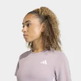 Remera deportiva Adidas de entrenamiento, color lila, con cuello redondo y mangas cortas. Presenta el logo de la marca en el pecho y las icónicas tres rayas blancas en los laterales. Diseñada con tecnología de absorción de sudor y ajuste clásico.