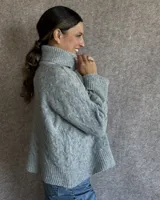 Sweater de lana color crudo con cuello alto y diseño trenzado.