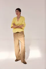 Pantalón de lino lavado de calce recto, color tostado, con cintas de lino desflecadas aplicadas en los costados con pespunte central. Cuenta con pretina de doble botón metálico, bolsillos delanteros y traseros, y ruedo al corte.