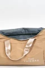 Bolso de viaje gris con doble asa corta y cierre superior. Estampado frontal con la frase "The Tote Bag" en letras blancas.