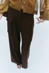 Pantalón cargo de tiro medio en color marrón oscuro, con corte recto y amplio. Presenta bolsillos laterales tipo cargo con solapa y detalle de pliegues frontales. Cierre frontal con cremallera y botón.