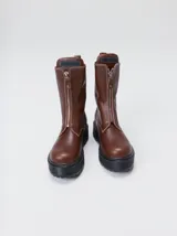 Botas de cuero color marrón de caña alta, con plataforma gruesa de goma y cierre metálico frontal con tirador. Presentan costuras a contratono y detalle de etiqueta de la marca en la lengüeta.