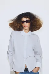 Camisa de algodón con estampado de rayas verticales, cuello solapa y puños en color blanco a contraste. Presenta cierre frontal con botones, bolsillo de plastrón en el delantero y bajo asimétrico.