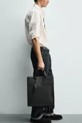 Bolso de hombro liso color negro, con cierre de imán en el compartimento principal y bolsillo interior con cremallera. Incluye un charm decorativo, dos asas de mano y un asa de hombro ajustable y extraíble.