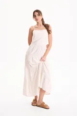 Vestido largo color blanco, confeccionado en lino, con tiras finas regulables, escote recto y falda amplia de corte acampanado con volados escalonados.