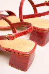 Sandalia de cuero vacuno color negro con textura de cocodrilo, taco cuadrado de 4 cm, punta cuadrada y dos tiras finas, una en el empeine y otra con hebilla en el tobillo.