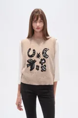 Chaleco de punto sin mangas en color beige con efecto confetti y diseño de jacquard frontal en color negro con motivos de herradura, luna y pájaro. Cuenta con cuello redondo y acabados acanalados.