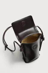 Bandolera porta teléfono de piel marrón con acabado liso, compartimento principal con solapa imantada y asa de hombro ajustable con nudos.