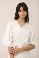 Bata corta color crema, confeccionada en algodón con elastano, con escote en V, mangas anchas y lazo para ajustar en la cintura.