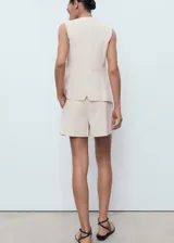 Short de tiro alto en color beige, con diseño recto, detalle de pinzas delanteras y bolsillos laterales. Cuenta con cierre oculto de botón, gancho y cremallera.