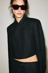 Blazer corto de lino color beige, con cuello redondo y cierre frontal cruzado con un botón negro.