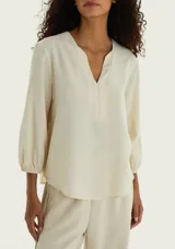 Blusa de viscosa color beige con escote en V y diseño con solapa frontal. Cuenta con mangas tres cuartos abullonadas con puños elastizados y dobladillo inferior curvado.