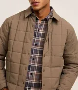 Campera marrón claro para hombre, confeccionada en tejido capitoneado de poliéster. Tiene cuello polo, manga larga con puños ajustados, abotonado delantero y bolsillo en el pecho.
