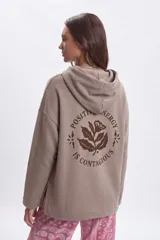Canguro deportivo de corte oversize en color taupe, con capucha y estampa gráfica en la espalda con diseño floral y la frase Positive Energy Is Contagious.