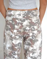 Pantalon de corte recto con estampado camuflado en tonos neutros, beige y marron. Presenta costuras verticales frontales que recorren el largo de las piernas, bolsillos laterales y cierre frontal con boton.