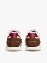 Zapatillas Tommy Hilfiger de estilo retro con paneles de ante y tela en tonos beige, marrón y naranja. Presentan suela gruesa dentada de goma, cierre con cordones y detalles de la marca en la lengüeta y el talón.