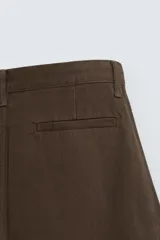 Pantalón de algodón color marrón oscuro, estilo balloon fit, con talle alto, cierre frontal y trabillas ajustables en los bajos. Presenta costuras verticales marcadas en el frente de cada pierna.