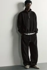Pantalón jogger de corte relajado en color negro, confeccionado en tejido con elasticidad. Presenta cintura elástica con cordón ajustable y bolsillos laterales decorados con tachas metálicas.