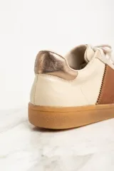 Zapatillas bajas color crema con puntera de gamuza beige, detalle de franja lateral en cuero marrón y contrafuerte en cuero metalizado color cobre.