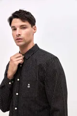 Camisa de corte regular confeccionada en algodón, con diseño de rayas verticales finas en color beige y negro. Presenta cuello clásico, cierre frontal con botones y un bolsillo en el pecho con el logo de la marca bordado.