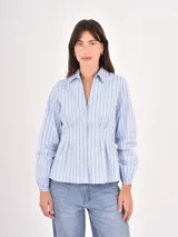 Camisa de corte entallado con pinzas en la cintura, cuello clásico y mangas largas con puños elásticos. Presenta un diseño a rayas verticales finas en color celeste sobre fondo claro.