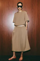 Top de nylon color tostado, con cuello redondo, mangas cortas y bajo abullonado ajustable con cordón y stoppers. Presenta cierre en la espalda con botón.