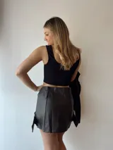 Minifalda marrón de cuero sintético con cierre frontal y cinturones cruzados con hebillas metálicas.