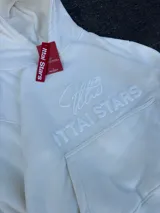 Hoodie de color blanco off-white con diseño de capucha, bolsillo frontal tipo canguro y bordado en relieve con el texto ITTAI STARS y un logo caligráfico.