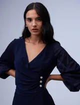 Vestido azul de RM Richards en seda fría, con escote en V cruzado, cintura drapeada, mangas largas de gasa y aplique de botones en el lateral.