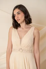 Vestido largo de gasa color champagne, con escote en V profundo y breteles anchos. Presenta una faja bordada con pasamanería y piedras en la cintura.
