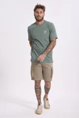 Remera de algodón color verde salvia, con cuello redondo y manga corta. Presenta un pequeño parche estampado en el pecho con un diseño gráfico.