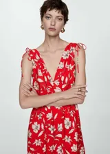 Vestido largo de tejido fluido con escote en pico cruzado y diseño evasé. Presenta tirantes anchos con detalle de lazos ajustables en los hombros y estampado floral en tonos rojos y crema.