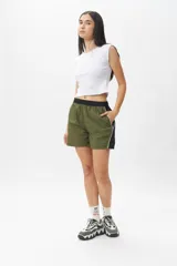 Short deportivo negro con detalles en verde militar, cintura elastizada, bolsillos laterales y ribete blanco.