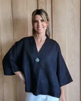 Camisaco de lino negro con cuello en V, cierre frontal con un único botón grande y mangas tres cuartos anchas.