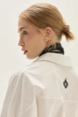 Camisa blanca de corte oversize, confeccionada en algodón, con cuello clásico y cierre frontal de botones. Presenta un bordado de corazones en el pecho.