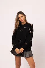 Buzo negro de cuello redondo con detalle de ojalillos metálicos plateados distribuidos en el frente y las mangas. Diseño de corte relajado con terminaciones acanaladas en cuello, puños y ruedo.