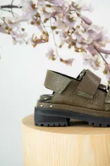 Sandalias negras de cuero con diseño de plataforma dentada, tiras ajustables con hebillas metálicas y detalle de tachas plateadas en el lateral de la suela.