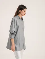 Camisa oversized con terminación metalizada color gris plomo. Tiene botones a tono en el delantero, largo por debajo de la cadera y tajos a los costados.