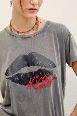Remera de algodón gris con efecto acid wash, mangas cortas y estampa frontal de labios oscuros con la palabra "Kiss" en rojo.