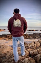 Hoodie marrón con capucha, corte oversize y estampado de paisaje montañoso en la espalda con la frase "Never Stop Exploring".
