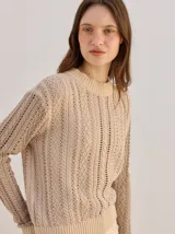 Sweater de punto color beige, de diseño atemporal con cuello redondo, mangas largas y terminaciones acanaladas.